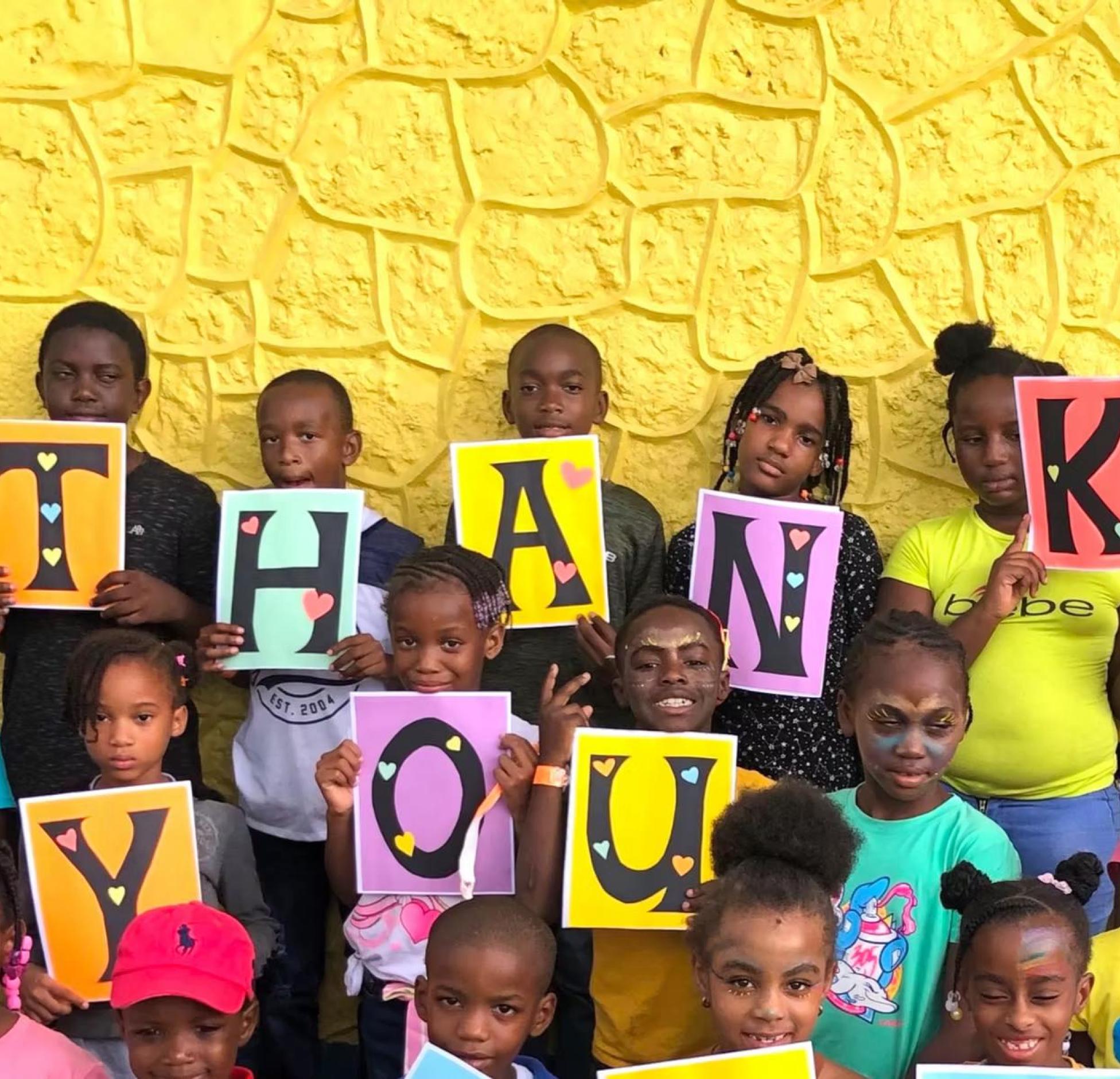 The image shows a group of children holding up letters that spell out 'THANK YOU' in front of a yellow wall. The purpose of the image is to express gratitude and appreciation.
